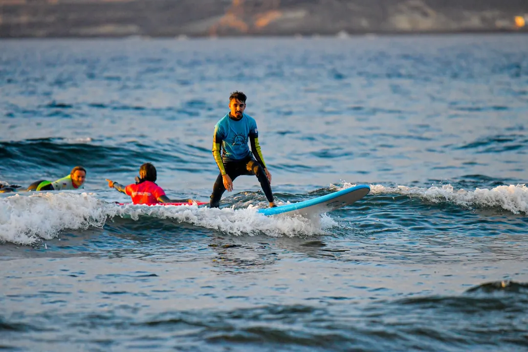 Clase de surf de Single Fin en Tenerife Surfista de pie sobre la tabla en una ola durante una clase de surf de Single Fin, con otros alumnos remando detrás