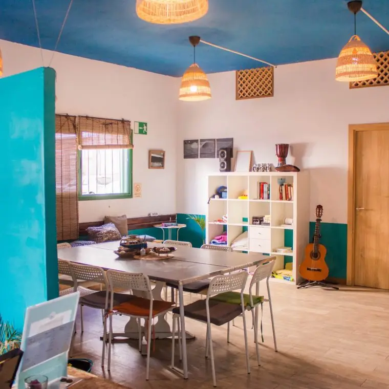 Sala común de Single Fin Surf Hostel con mesa grande, estantería y guitarra