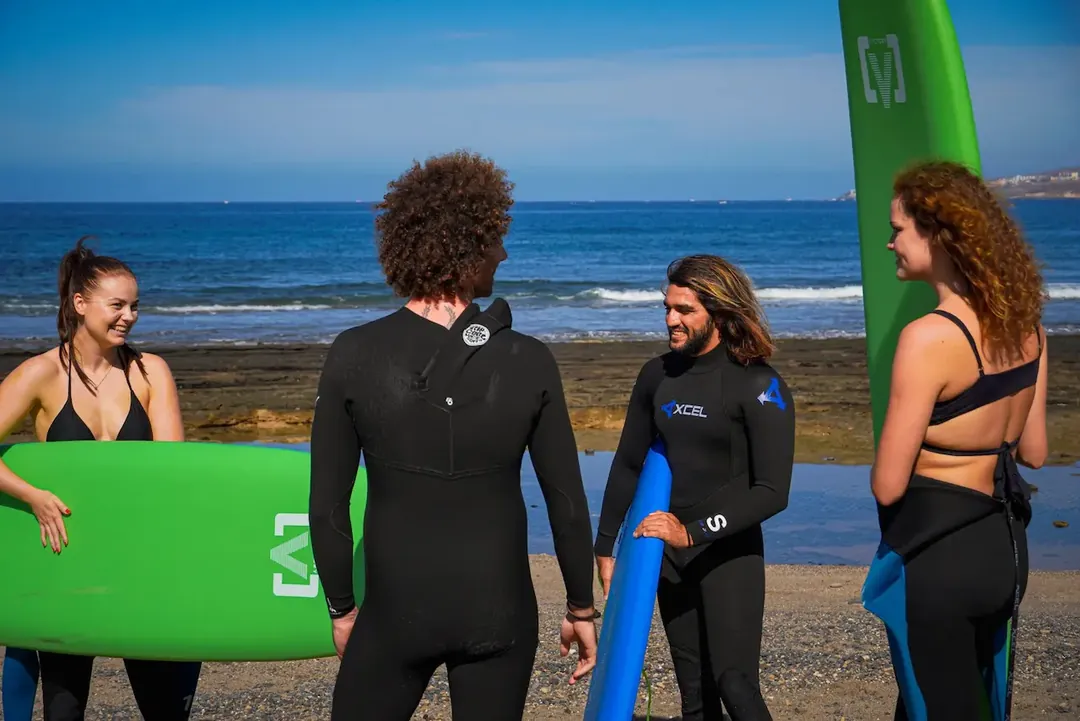 Equipo de Single Fin charlando con alumnas en la playa, con las tablas de surf y el mar de Tenerife al fondo