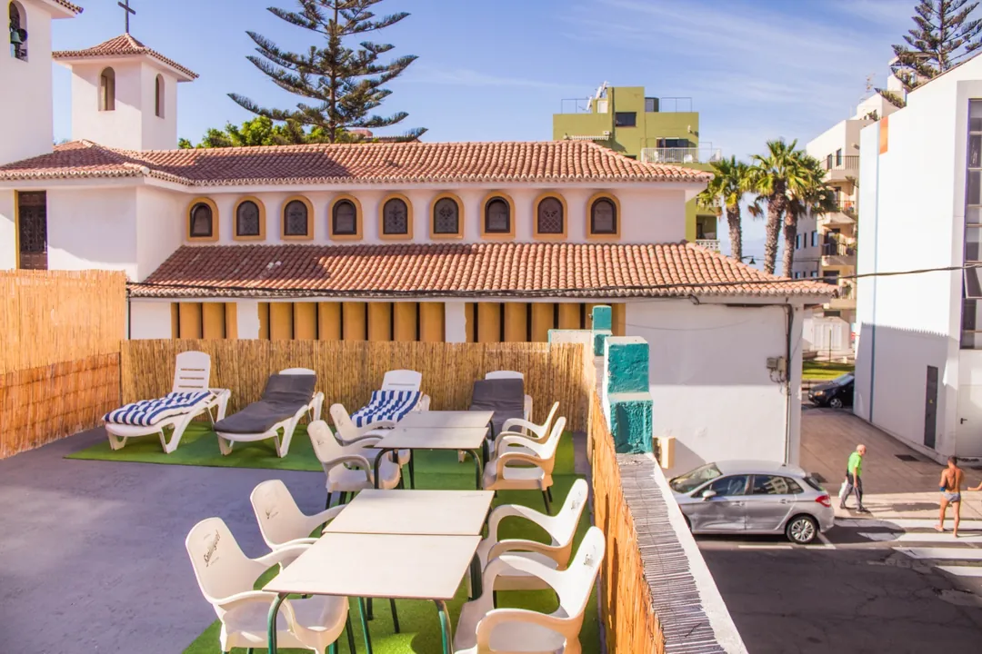 Terraza soleada de Single Fin Surf Hostel con tumbonas, mesas y césped artificial
